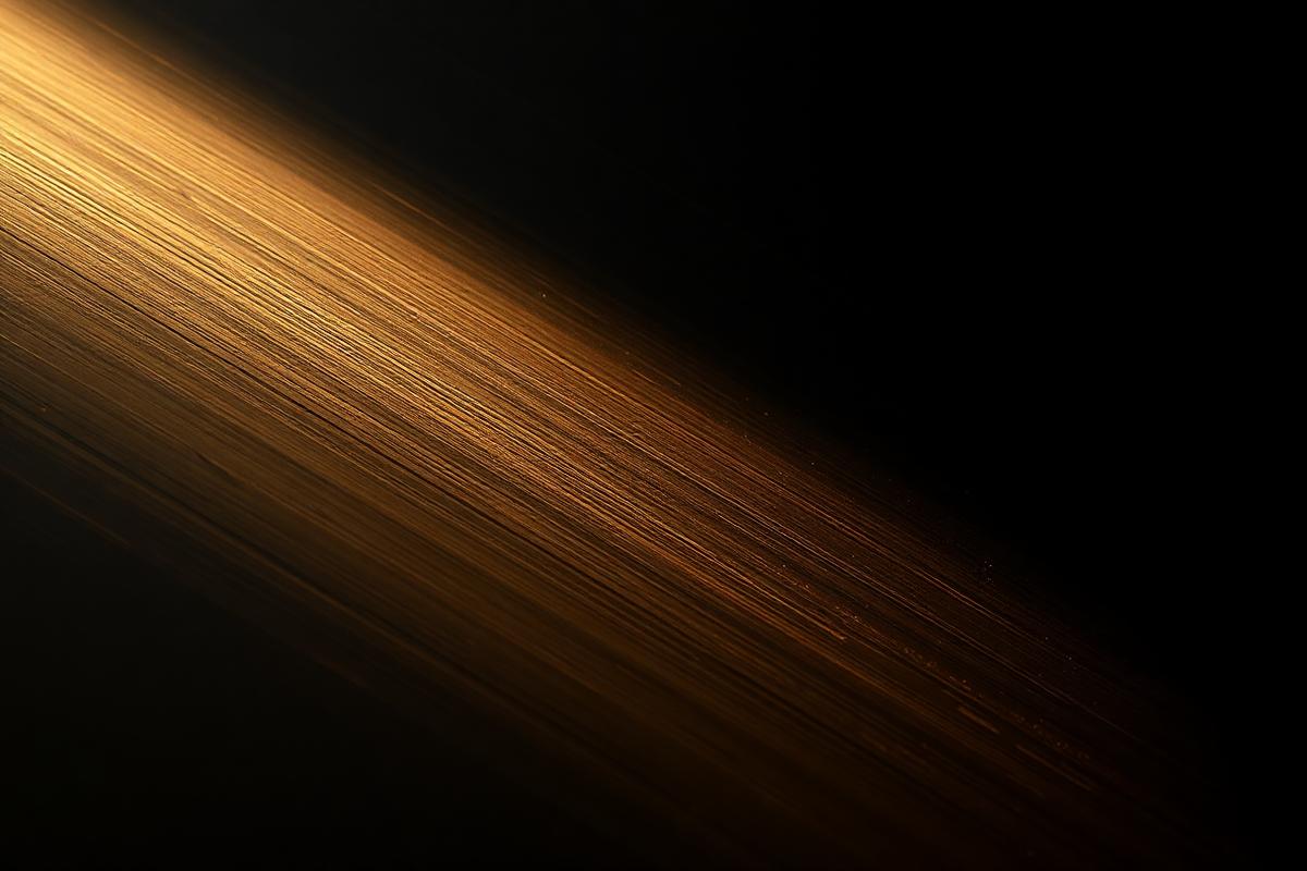 Macro brushed brass catching a sharp highlight against deep charcoal